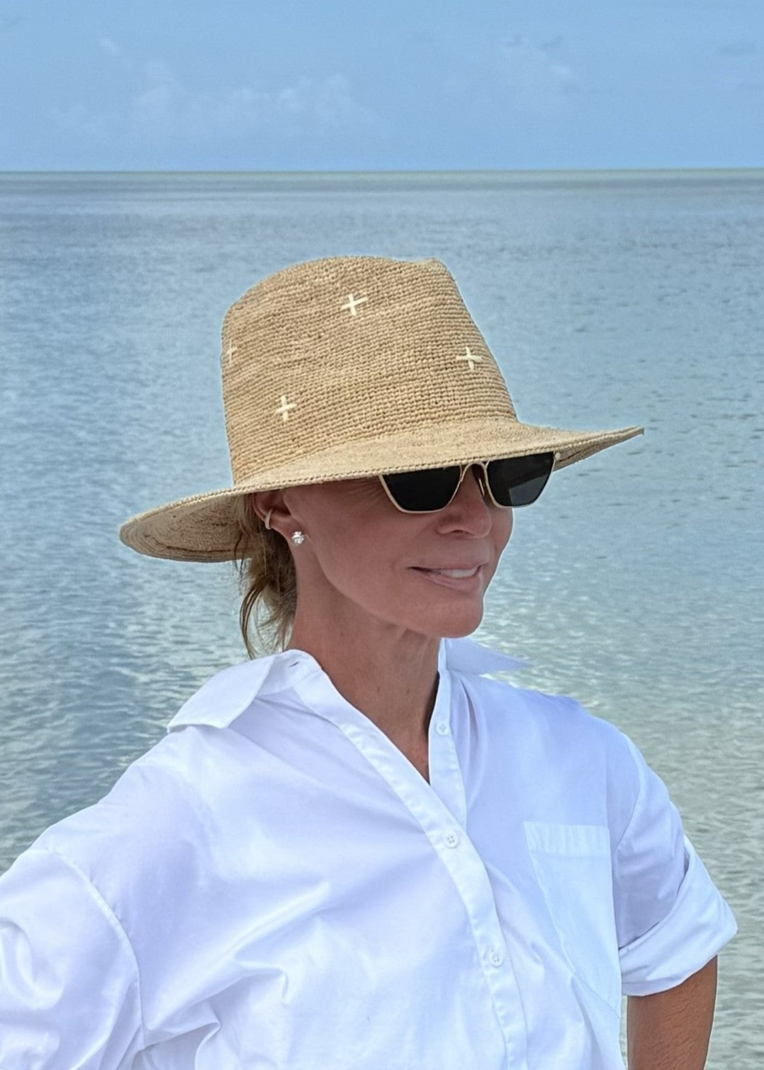 Person wearing a straw hat and sunglasses with a body of water in the background