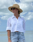 Person wearing a white shirt, straw hat, and sunglasses on a beach with blue sky and ocean.