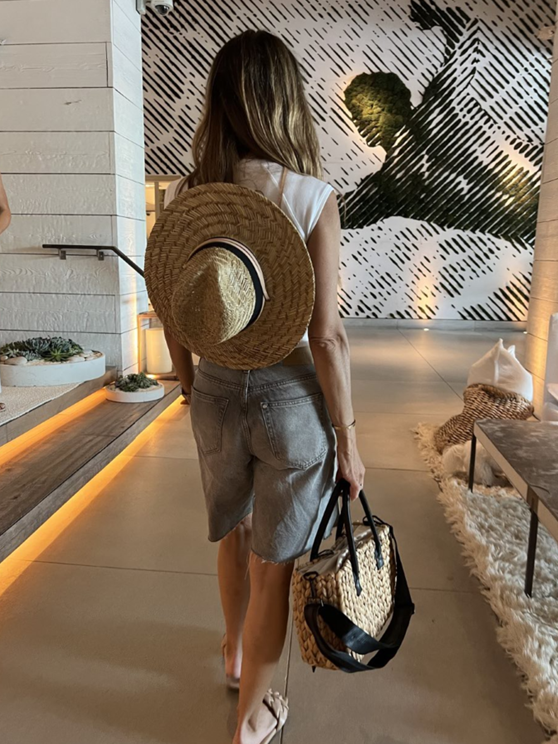 person wearing the tower hat and holding the gabie medium sized hyancinth straw bag with black leather handles and black crossbody strap