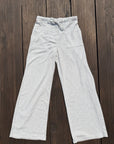 Light heather gray wide-leg sweatpants with a drawstring waistband and side pockets, laid flat on a dark brown wooden plank background.