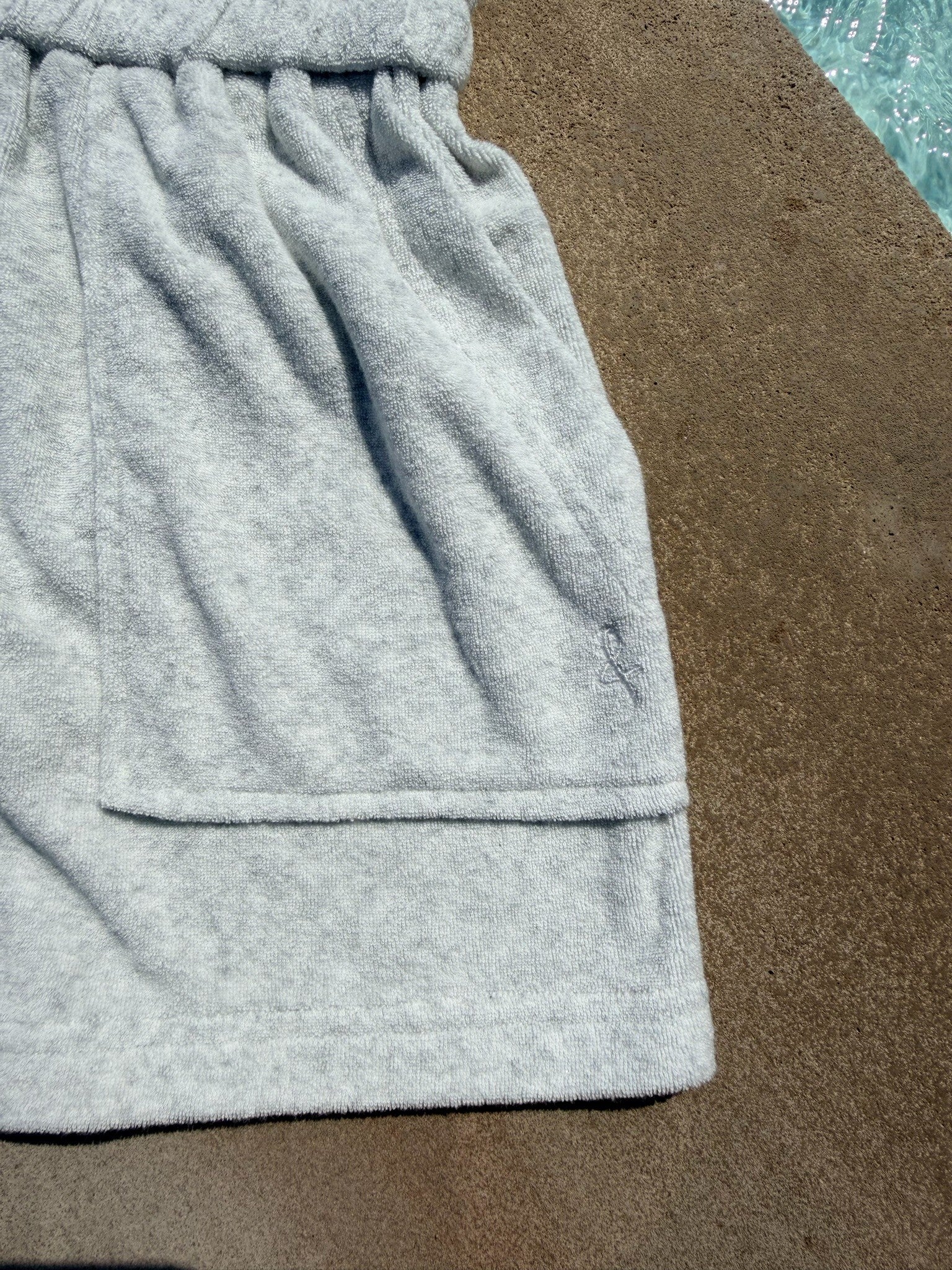 Close-up of a light gray heather sweatshirt or hoodie showing the fabric texture, waistband, and hem, laid flat on a brown surface.