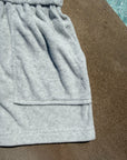 Close-up of a light gray heather sweatshirt or hoodie showing the fabric texture, waistband, and hem, laid flat on a brown surface.