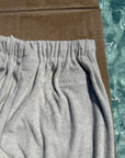 Close-up of light gray heather sweatpants with an elastic waistband, laid next to a brown towel and a swimming pool.
