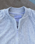 Close-up of a light heather gray zip-up sweatshirt with a ribbed collar, featuring a white zipper and a visible 'ANYA & NIKI' brand label.