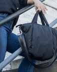 Person holding a mid-sized black nylon puffy tote with removable crossbody strap with leather detail