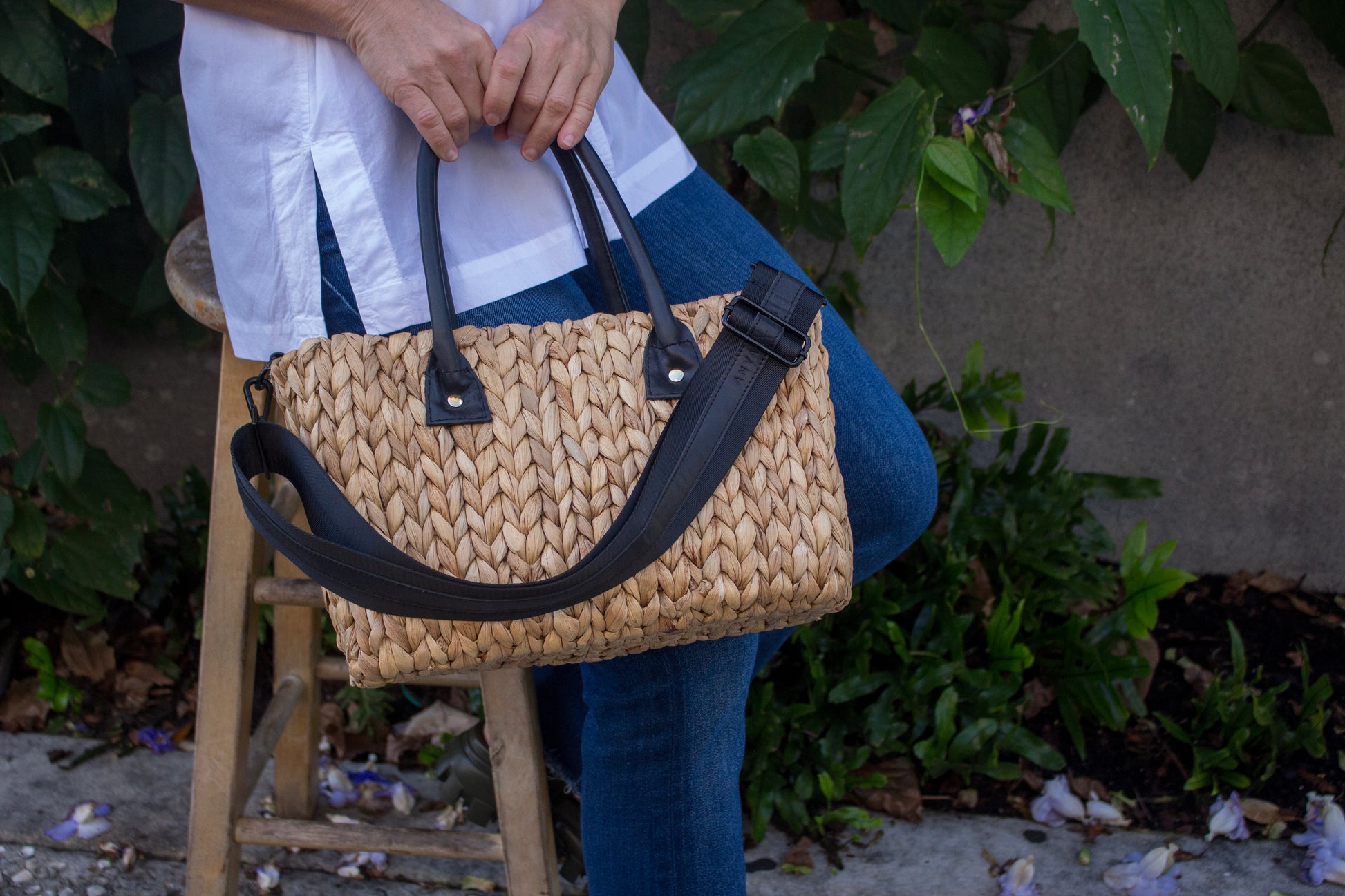 Person holding mid-sized hyancinth straw bag with black leather handles and black crossbody strap