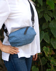 Person wearing denim belt bag with black crossbody/belt bag strap with black leather detail