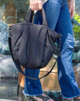 Person holding a mid-sized black nylon puffy tote with removable crossbody strap with leather detail