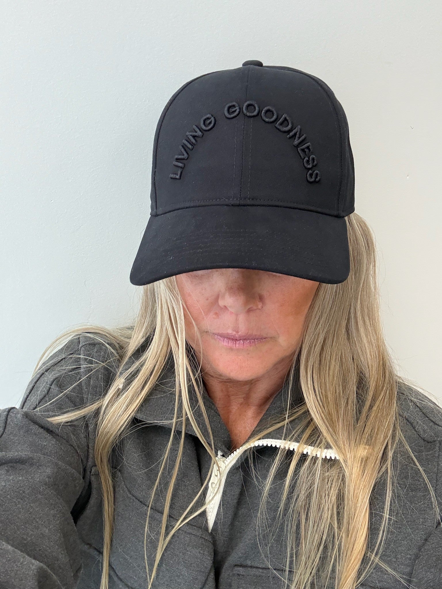 Person wearing a black cap with 'LIVING GOODNESS' text on a plain background