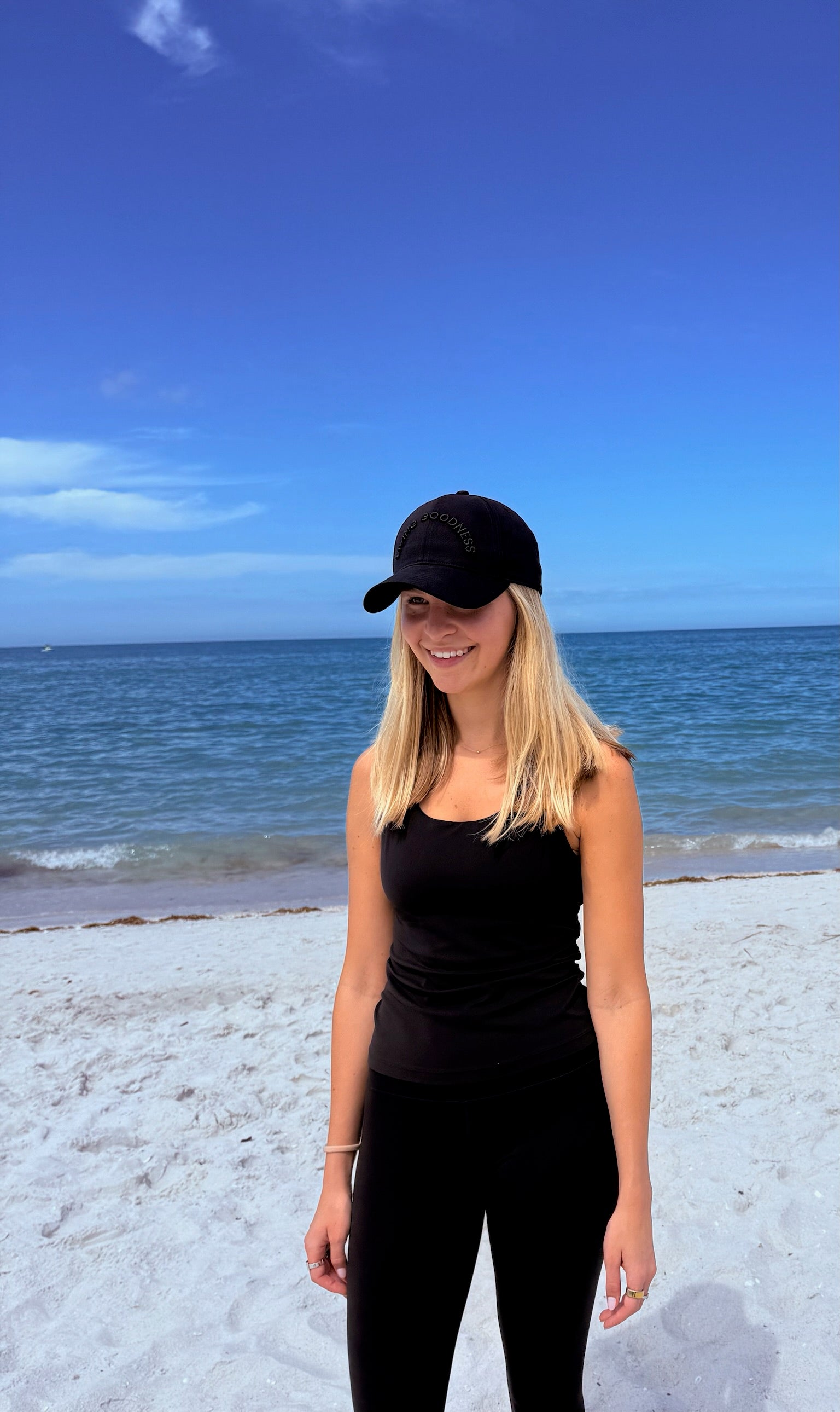 Person at the beach wearing a black outfit and black baseball cap
