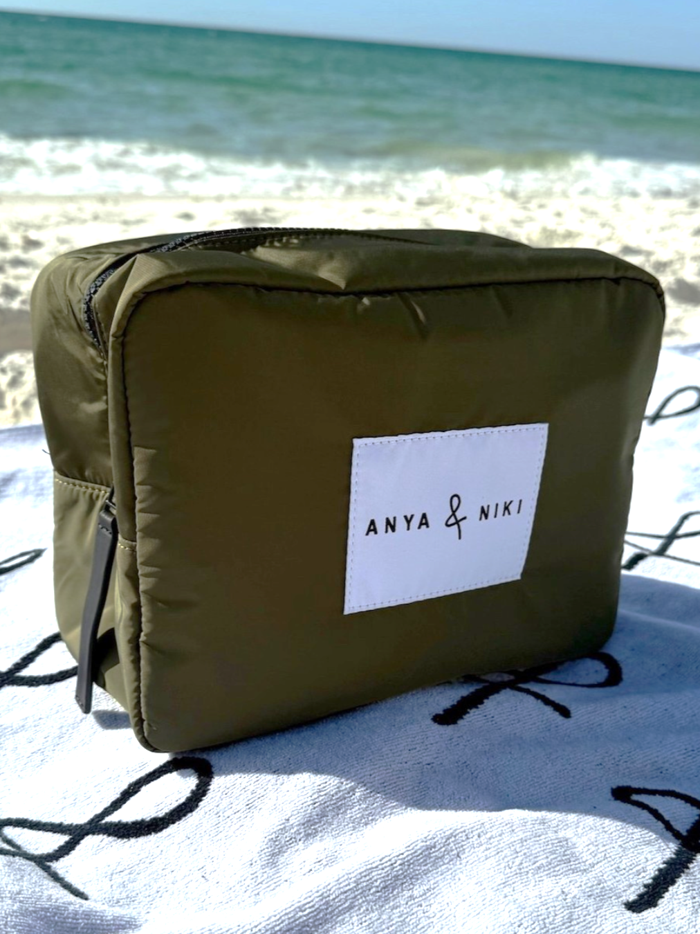 Green bag with 'Anya &amp; Niki' label on a sandy beach