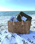 Woven bag with a towel and olive green pouch on a beach