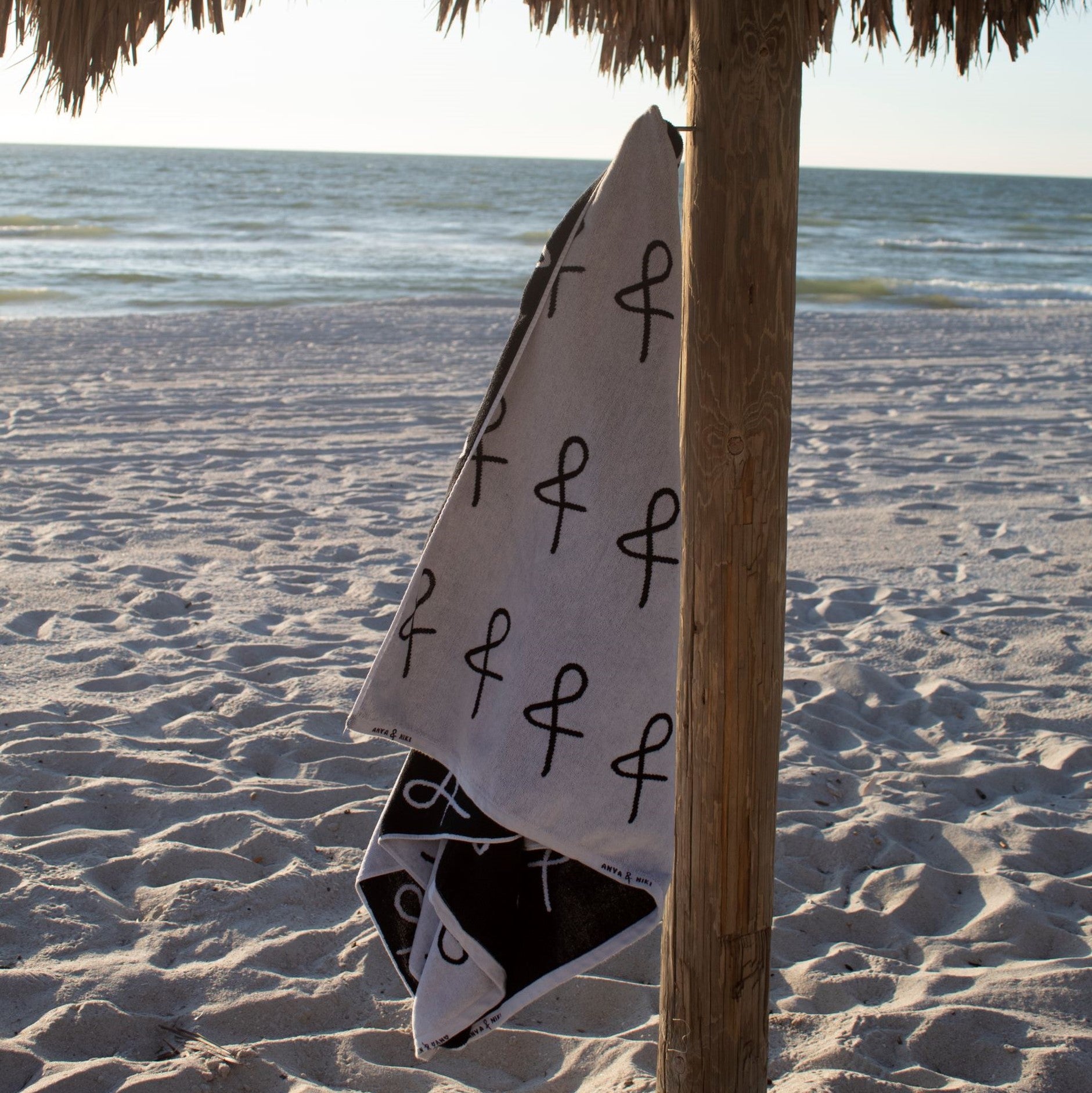 Anya &amp; Niki large beach towel hanging from a cabana pole at the beach