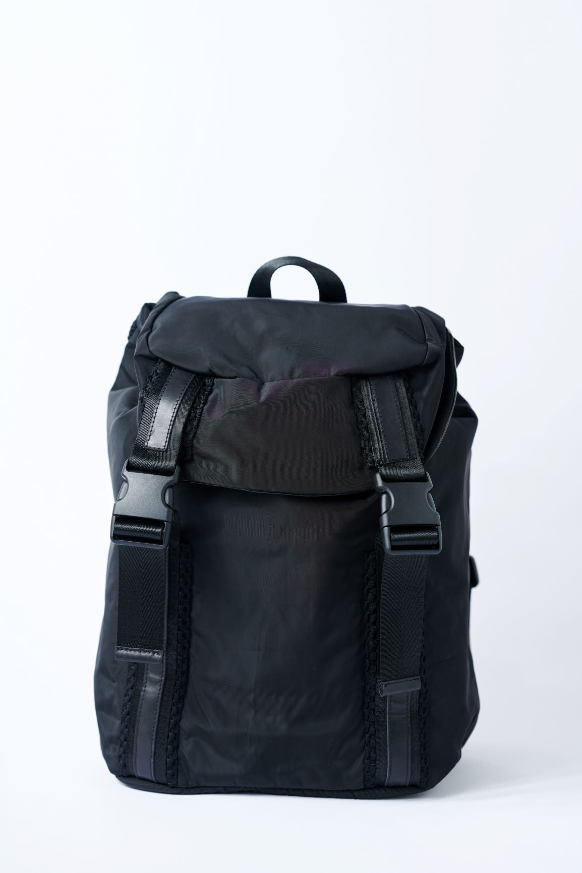 Black nylon flap top backpack with mesh and leather trim details and glossy black lining. 