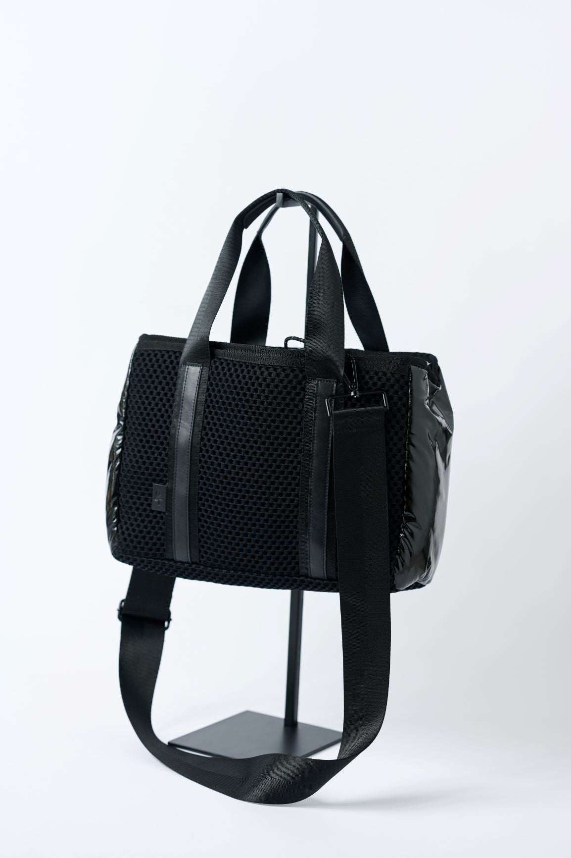 Small black mesh tote with glossy black sides, shiny silver cinch top and crossbody strap.