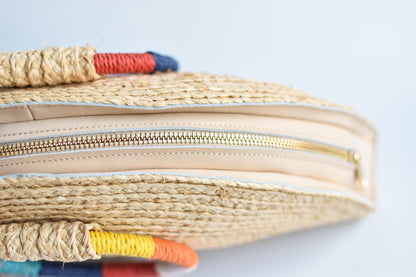 Top view of natural raffia straw half-moon clutch with rainbow colored wrapped circle handle and leather sides.