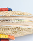 Top view of natural raffia straw half-moon clutch with rainbow colored wrapped circle handle and leather sides.