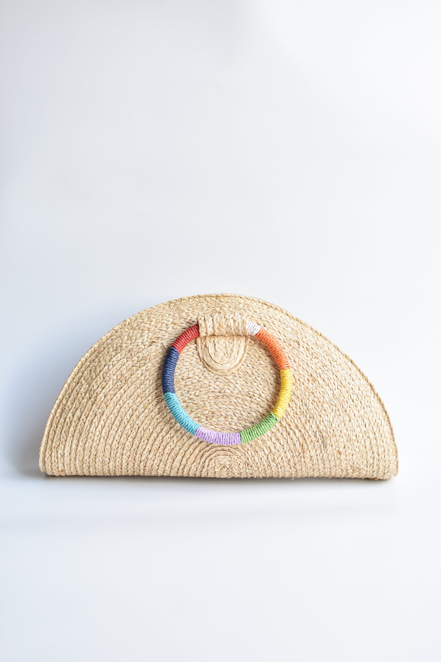 Natural raffia straw half-moon clutch with rainbow colored wrapped circle handle and leather sides.