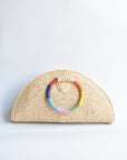 Natural raffia straw half-moon clutch with rainbow colored wrapped circle handle and leather sides.