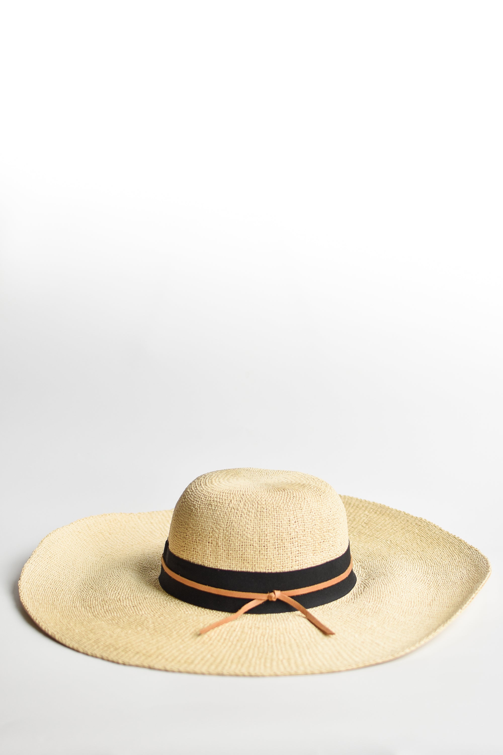 Natural floppy straw hat with black grosgrain ribbon and thin brown leather band.