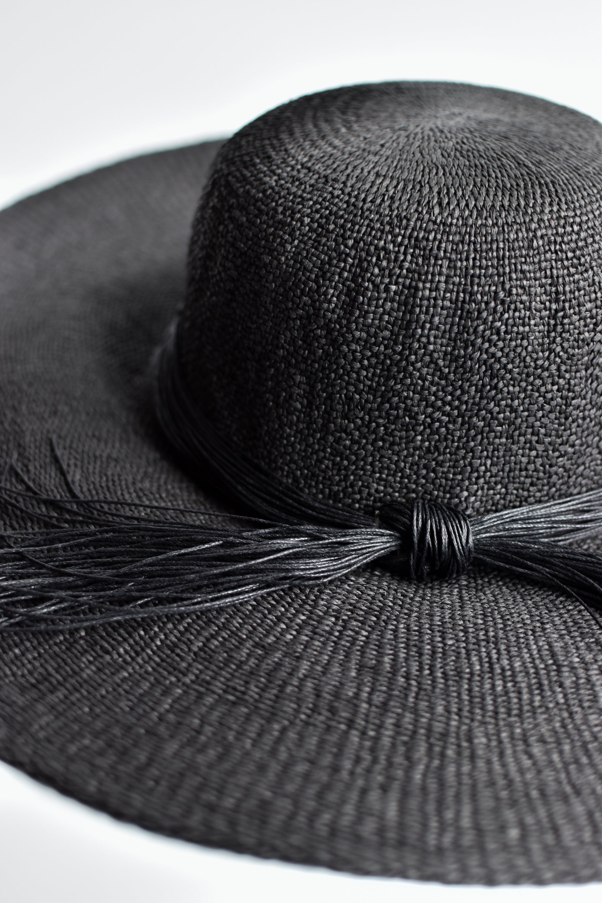 Close up of black floppy straw hat with multi-strand black cording band.