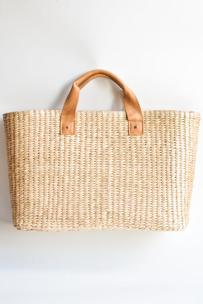 Large straw tote bag finished with natural leather handles and linen lining. 