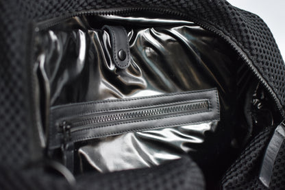 Close up of interior black glossy lining on black mesh duffel bag with leather trim details. 