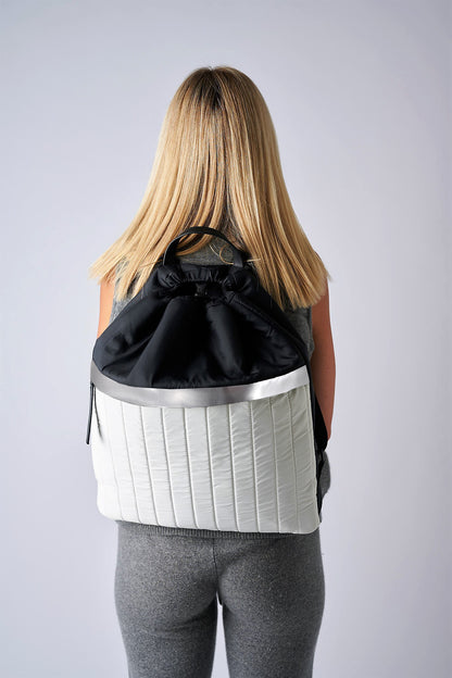 Person wearing black & white nylon cinch top backpack with signature leather and shiny silver details.