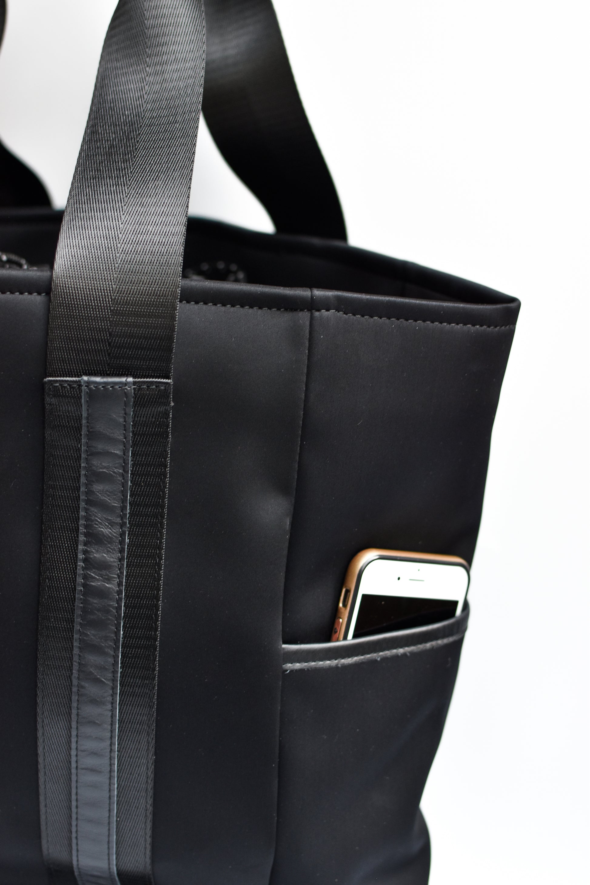 Close up of exterior pocket on black neoprene tote bag with high shine cinch top closure and leather details. 