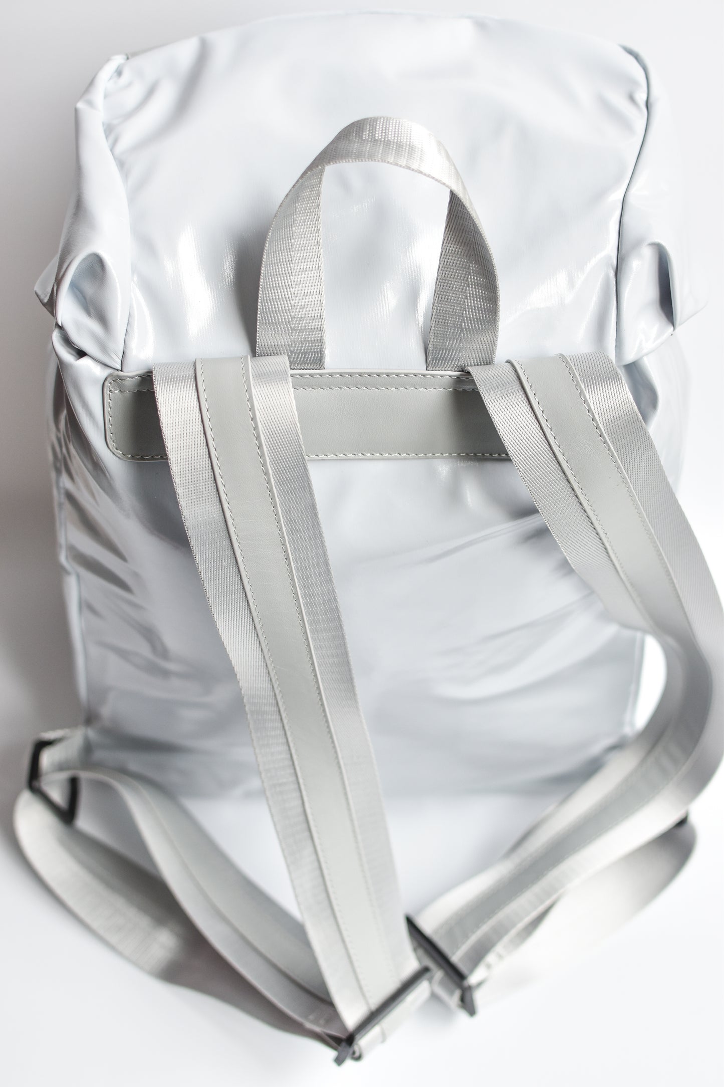 Back view of gray high gloss backpack with gray leather and webbing details. 