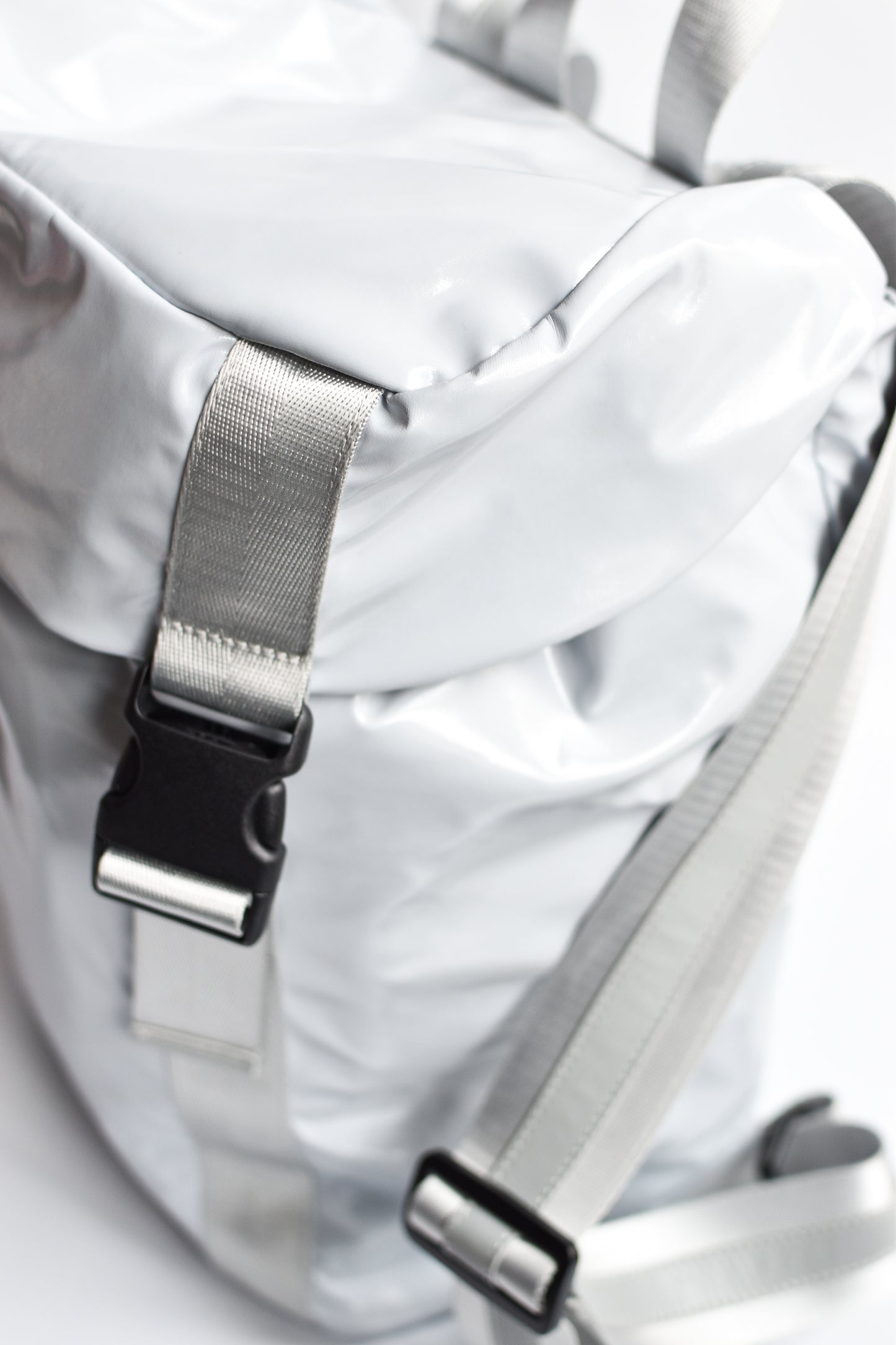 Side view of gray high gloss backpack with gray leather and webbing details. 