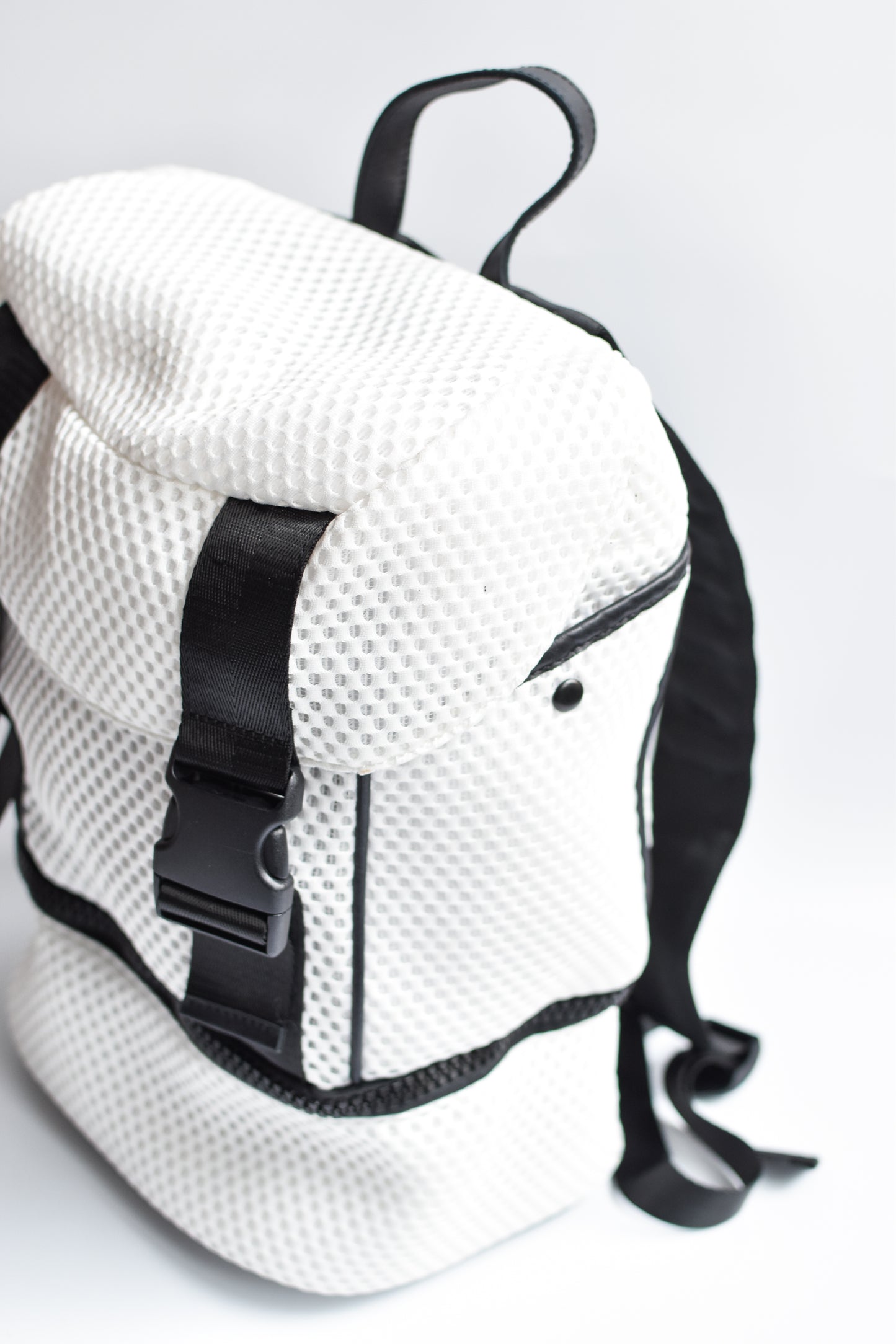 Side view of brooker white mesh backpack with black front straps and bottom zipper compartment with black chunky zipper. 