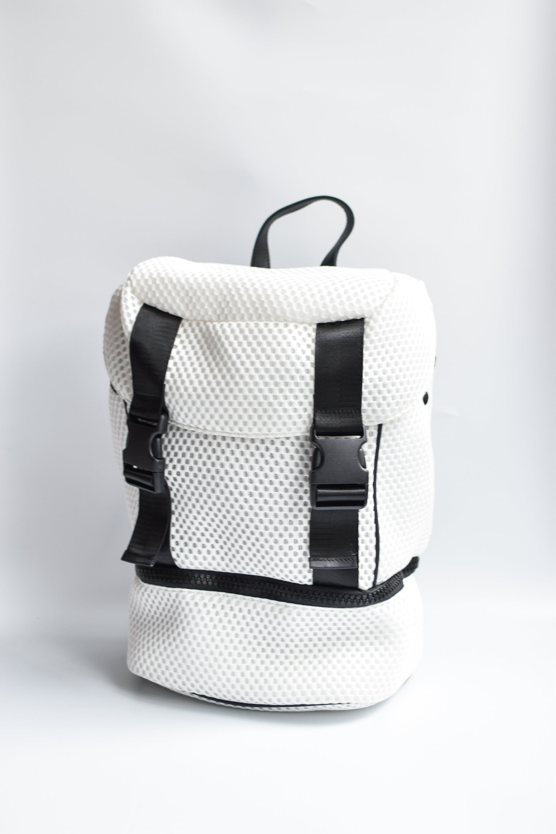 Brooker white mesh backpack with black front straps and bottom zipper compartment with black chunky zipper. 