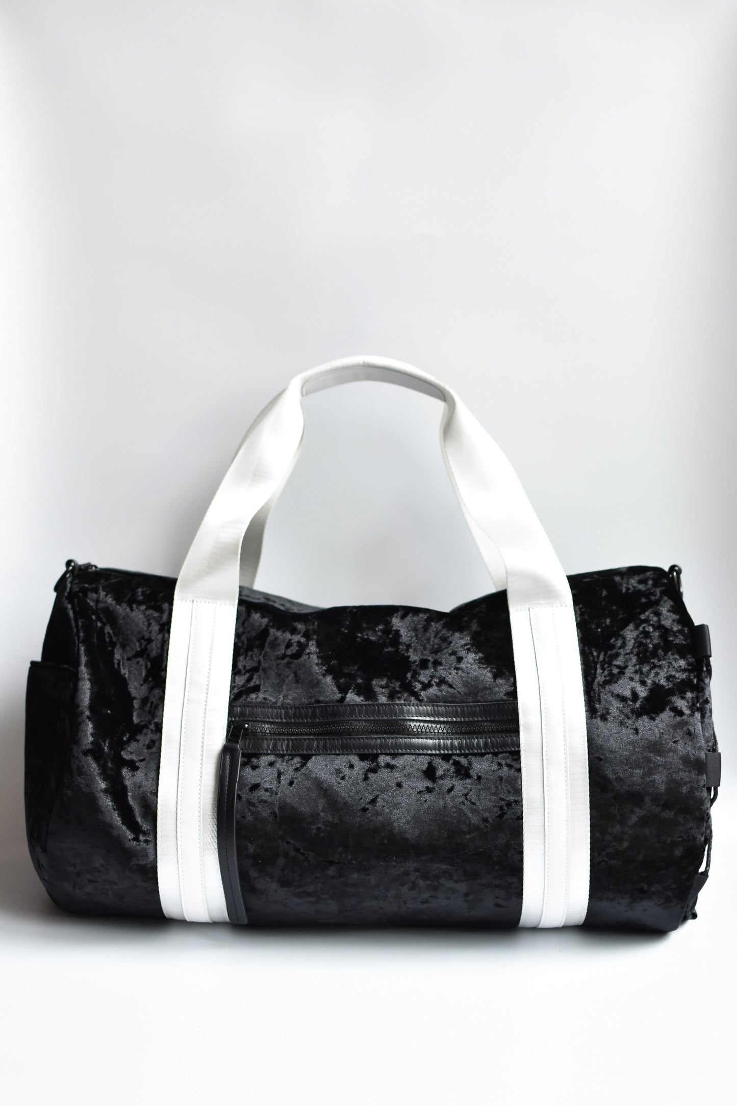 Black velour duffel bag with white straps and leather details. 