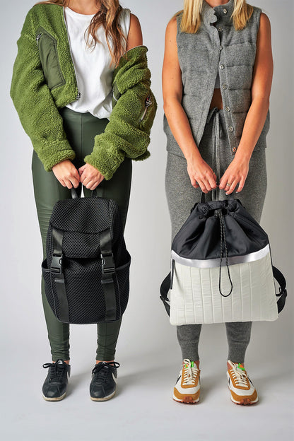 Two people holding Anya & Niki backpacks, including the Newberry black mesh backpack and the Pace black & white nylon cinch top backpack.