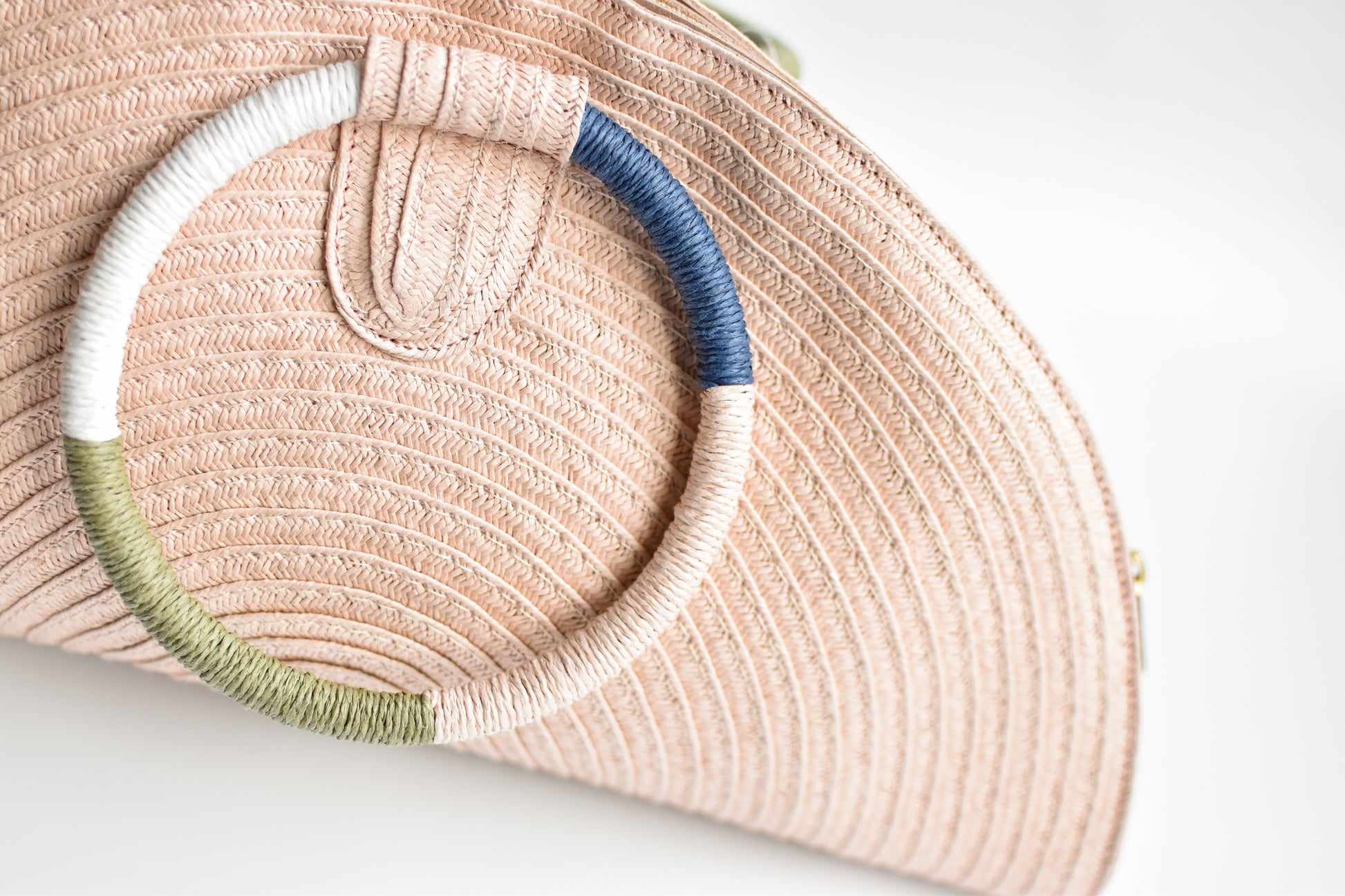 Pink half-moon straw clutch with colorful wrapped circle handle and leather sides.