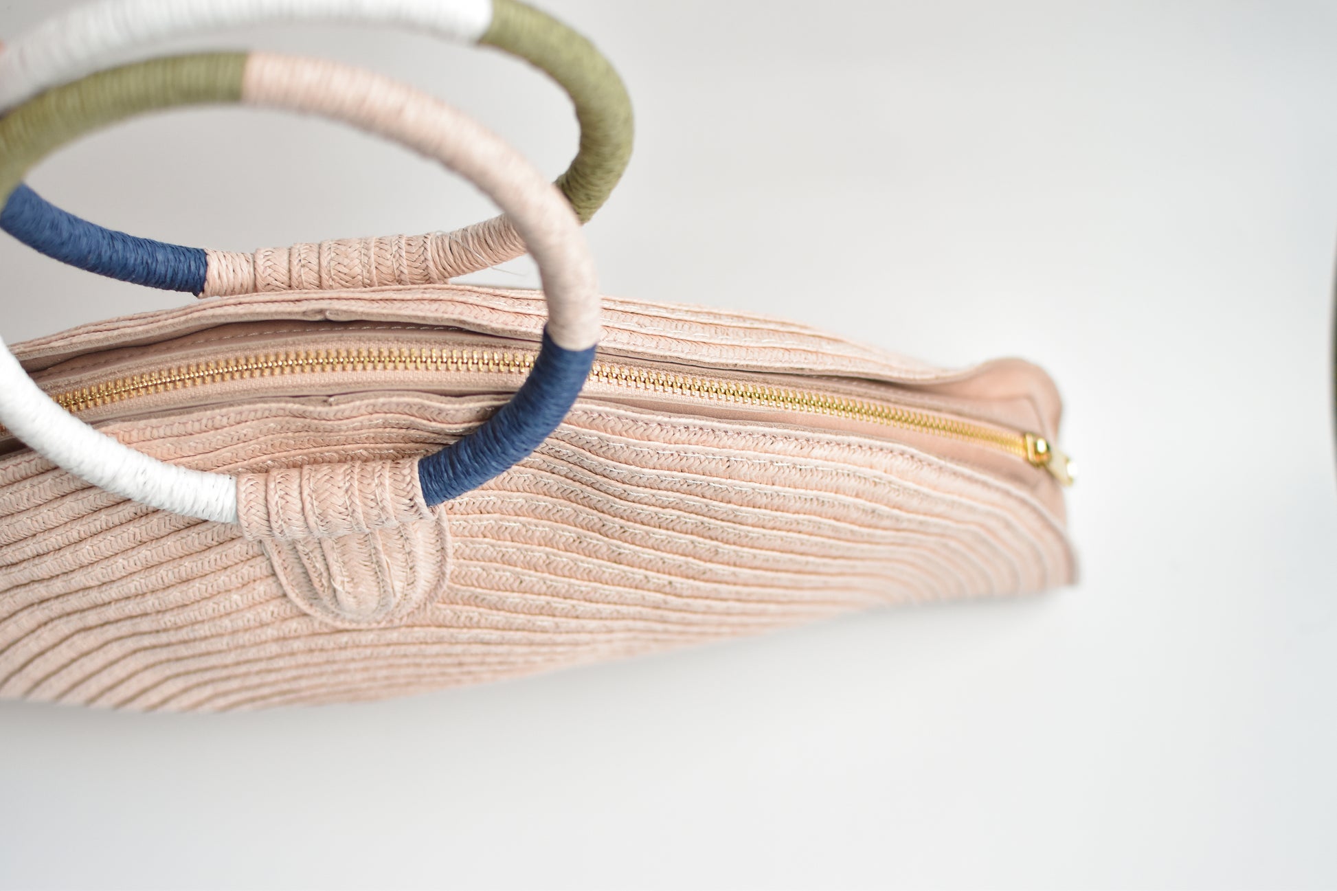 Top view of pink half-moon straw clutch with colorful wrapped circle handle and leather sides.
