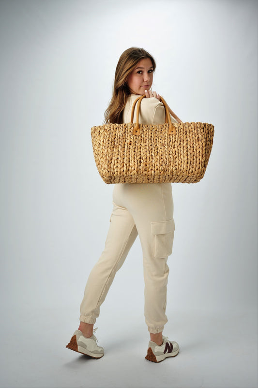 Person holding the Fullerton Straw Tote - a large natural hyacinth straw tote with matching leather handles.