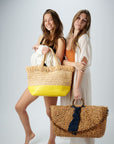 two people holding straw bags including a straw bag with fringe top and yellow bottom and a hyacinth straw bag with torte handle and strap