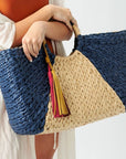 Person holding the Anya & Niki Isla straw bag - a navy and natural colored over-sized straw tote with circle handle and suede tassels.