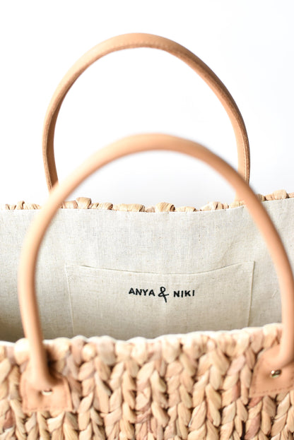 Close up of tan leather handles on large natural hyacinth straw tote. 