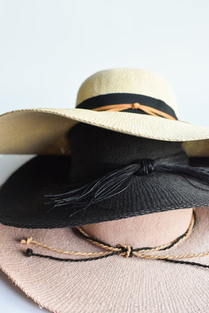 Stacked floppy straw hat collection, featuring a black floppy straw hat, pink floppy straw hat and natural colored floppy straw hat.