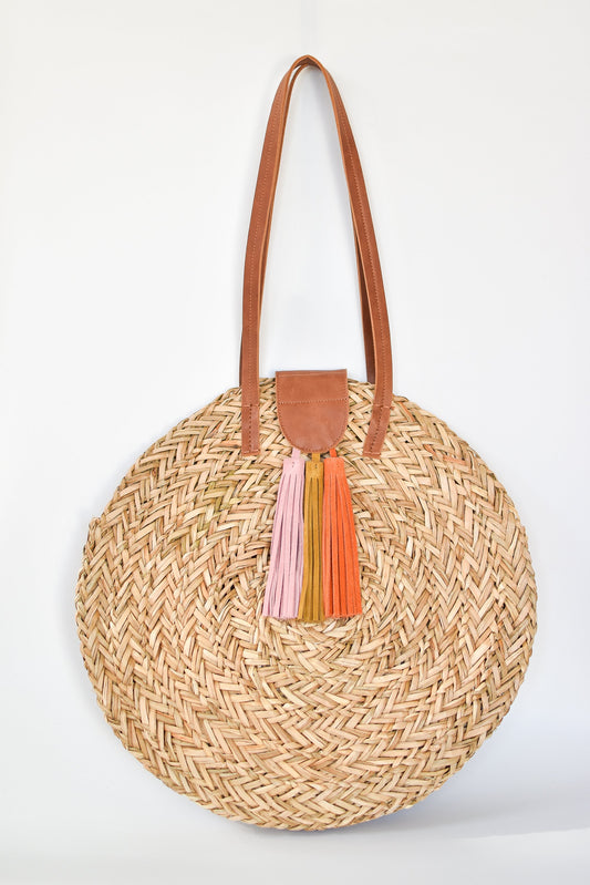 Natural seagrass round straw bag with leather handles and suede tassel closure. 
