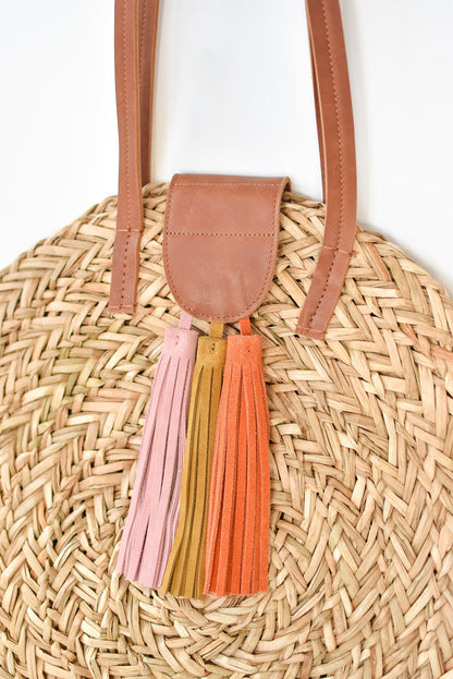 Close up of natural seagrass round straw bag with leather handles and suede tassel closure. 