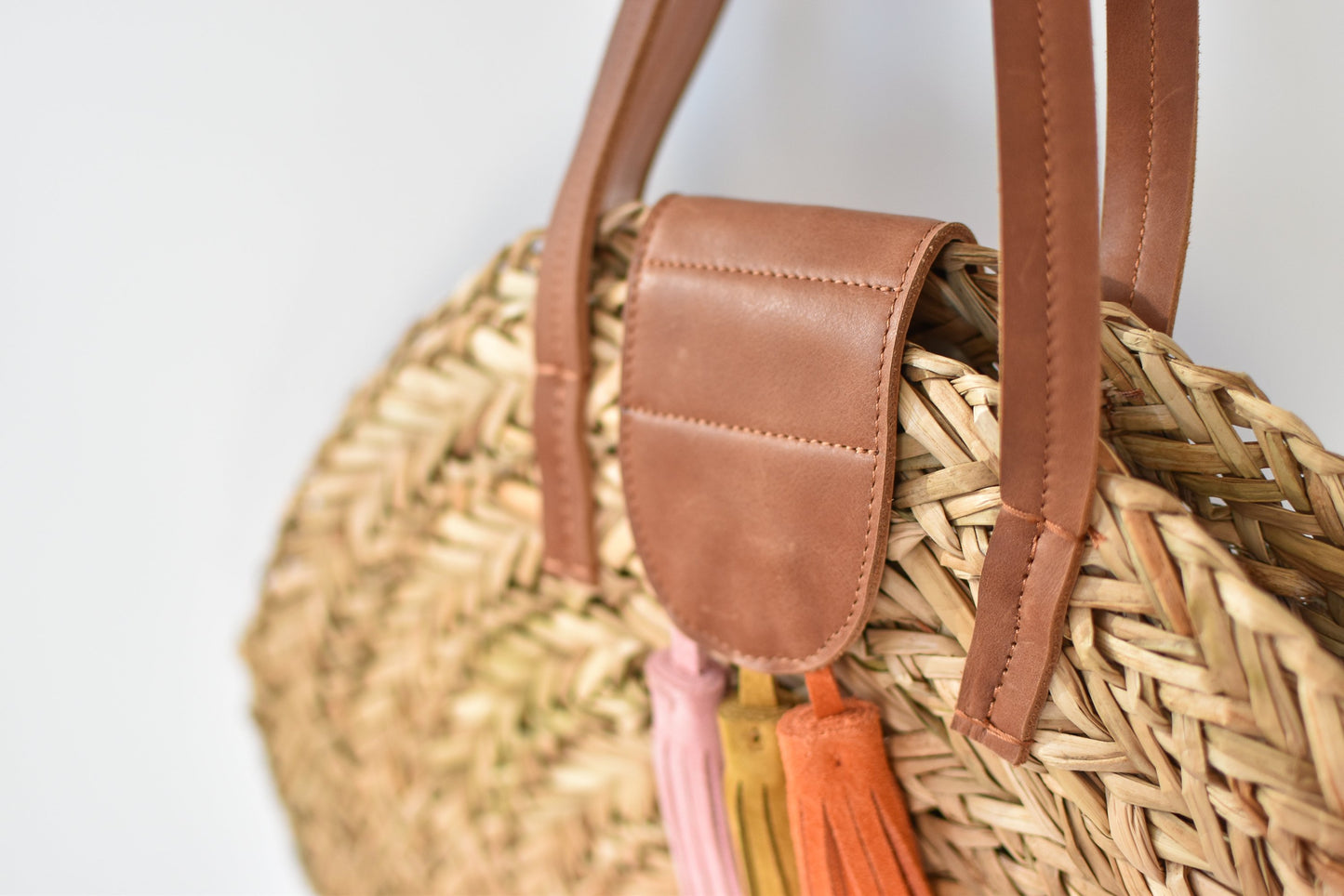 Close up of natural seagrass round straw bag with leather handles and suede tassel closure. 