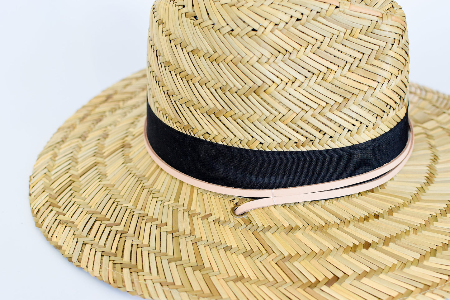 Close up of tan leather chin strap and black band detail on straw lifeguard hat. 