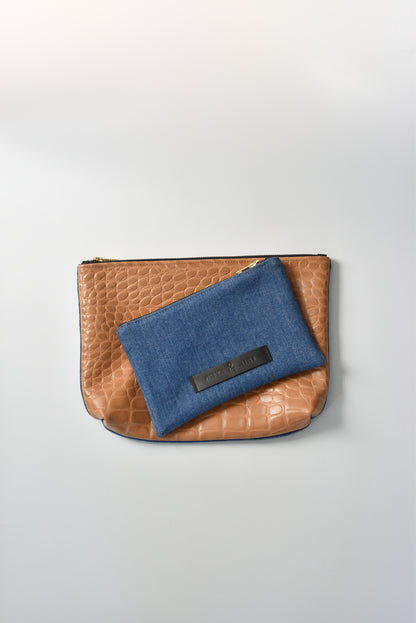 Medium wash denim and caramel colored embossed leather skin small and medium pouch with brass zipper and leather logo label.