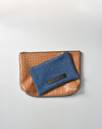 Medium wash denim and caramel colored embossed leather skin small and medium pouch with brass zipper and leather logo label.