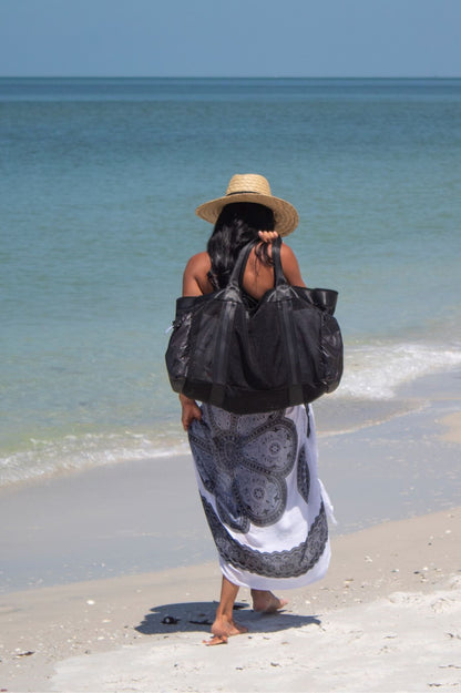 Person at beach holding large black mesh beach bag and wearing the straw Tower Hat with leather chin strap