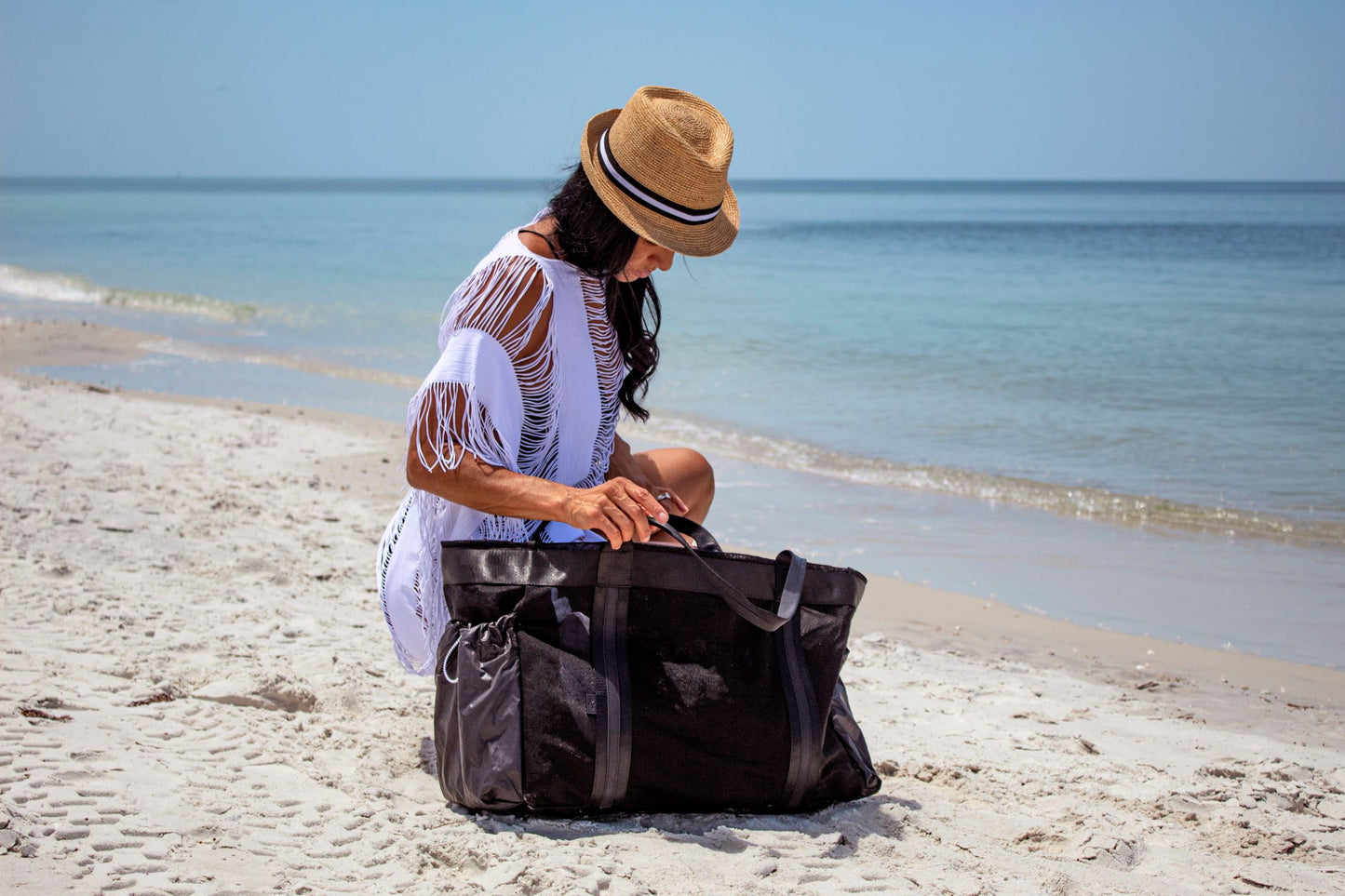 Person at beach wearing straw Essential Hat and looking into large black mesh bag